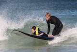 A boy and a man on a boogie board riding a wave at Trigg Beach.