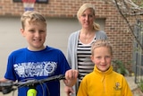 A mother and her two sons stand with a bicycle in the driveway of their home where they have been playing. 