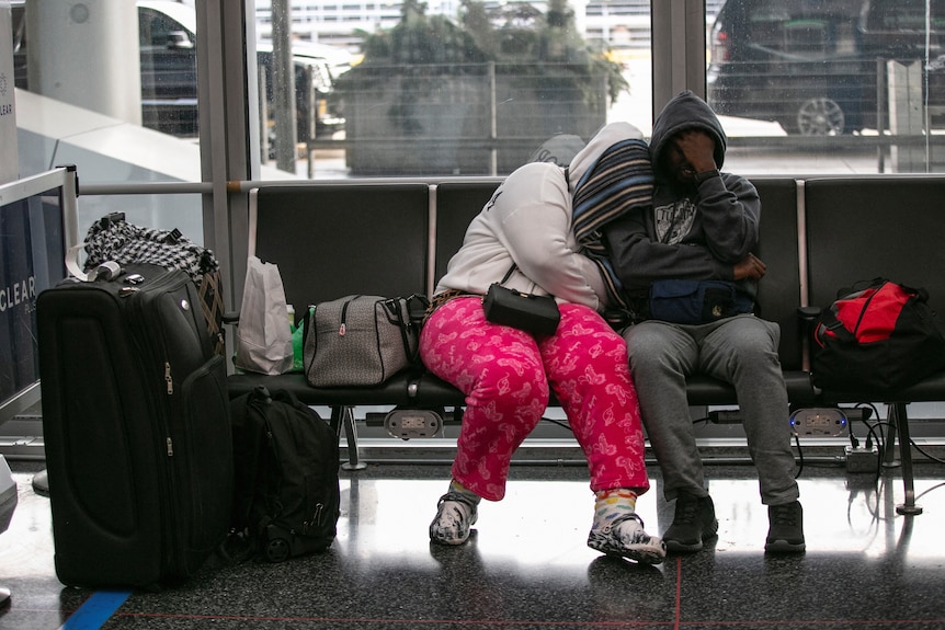 一男一女挤在机场的长椅上，穿着便服，身边放着行李。
