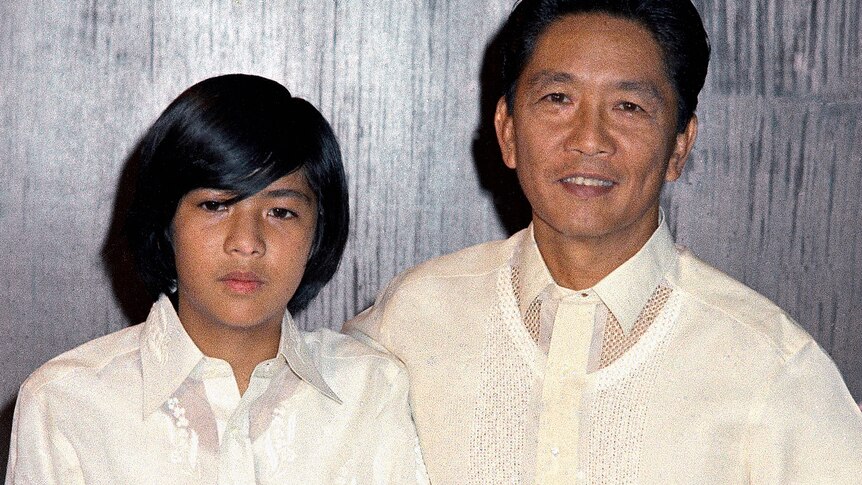 A young Bongbong Marcos in a white shirt standing next to his father, also dressed in a white shirt 