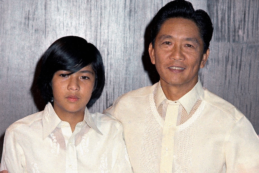 A young Bongbong Marcos in a white shirt standing next to his father, also dressed in a white shirt 