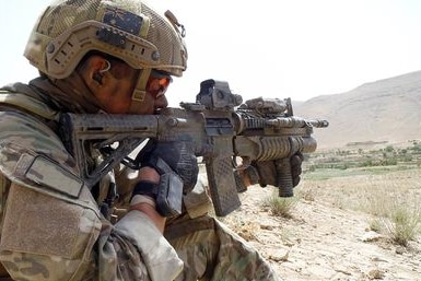 A soldier with an Australian flag on his helmet aims his weapon into the distance.