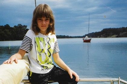 a young girl with brown hair wearing a colourful t-shirt sits on a boat.