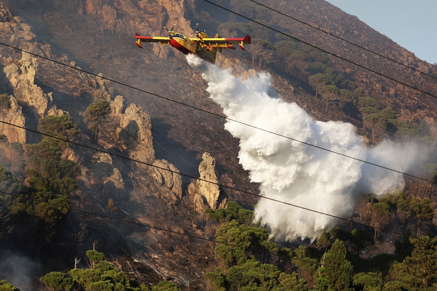 Yellow and red firefighting plane sprays water over mountains 