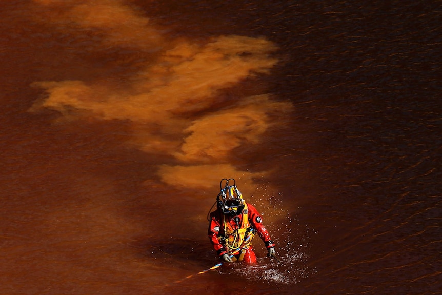  A diver walks out from a toxic man-made lake after a dive search for a third victim.