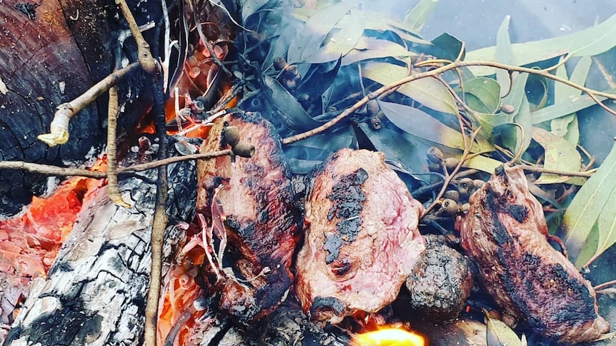 Kangaroo steaks are charred with leaves in a fire