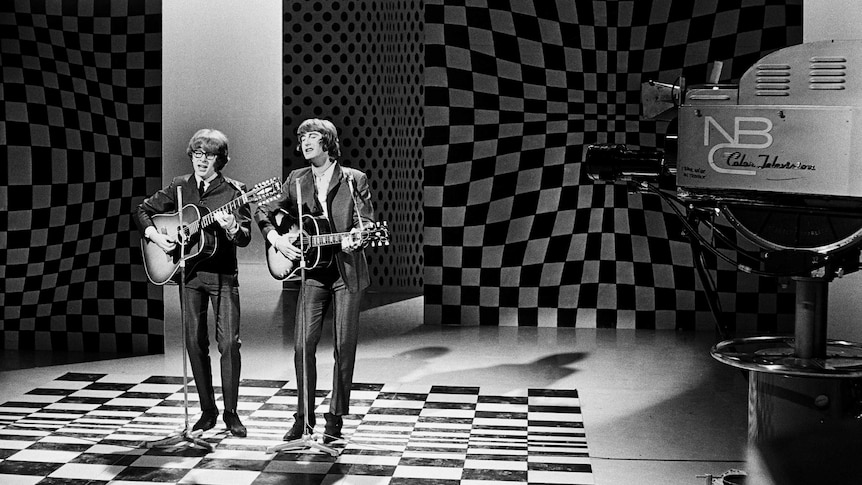 A black and white photo of Peter Asher and Gordon Waller singing and playing guitars in a television studio.