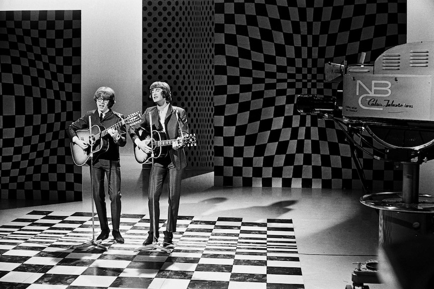 A black and white photo of Peter Asher and Gordon Waller singing and playing guitars in a television studio.