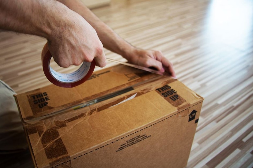 Man's hands tape up a box when moving house.