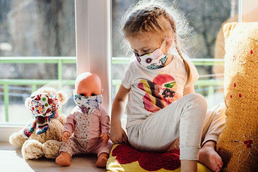 A child with her toy baby and teddy, all wearing masks