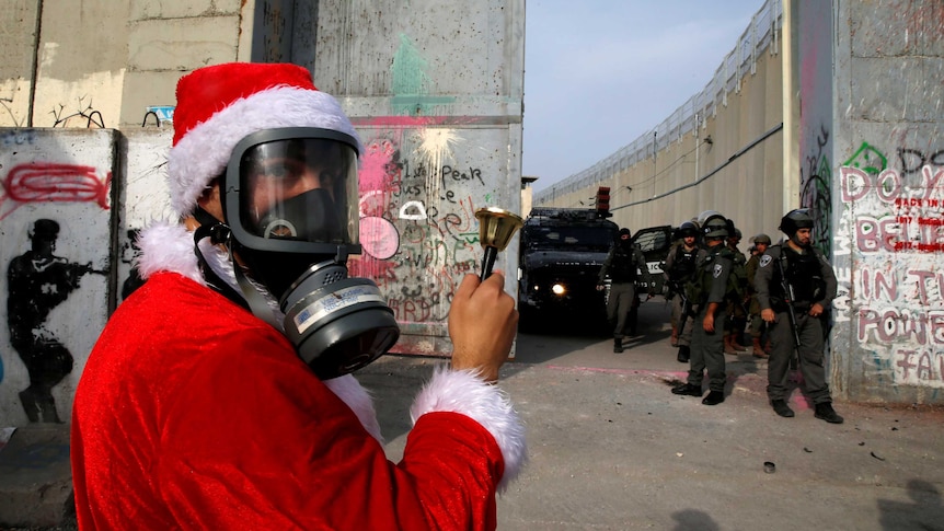 Palestinian demonstrator dressed as Santa stands in front of Israeli forces