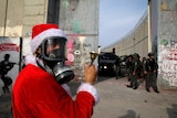 Palestinian demonstrator dressed as Santa stands in front of Israeli forces