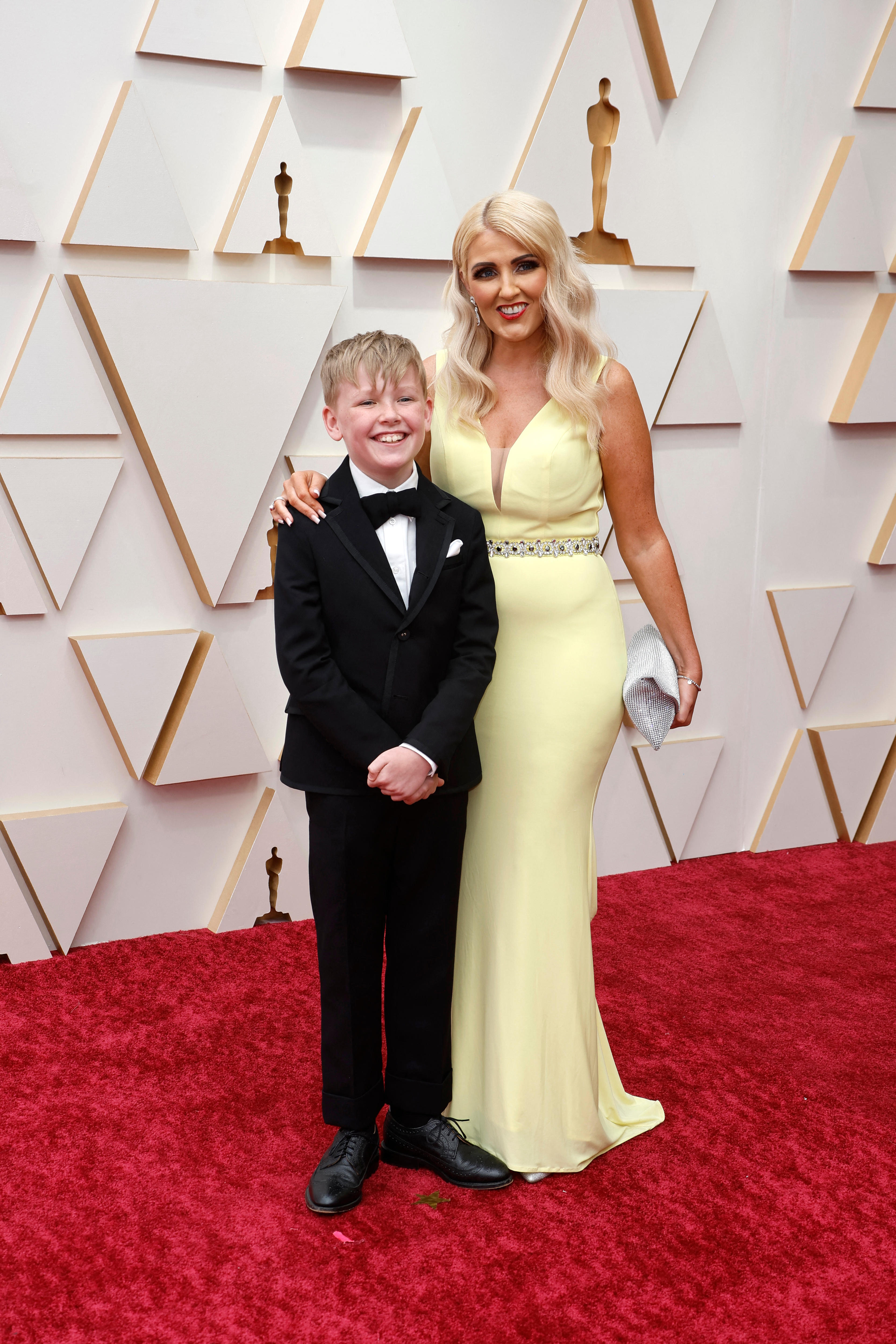 11 year old actor jude hill poses on a red carpet with his mother who is wearing a long pale yellow gown