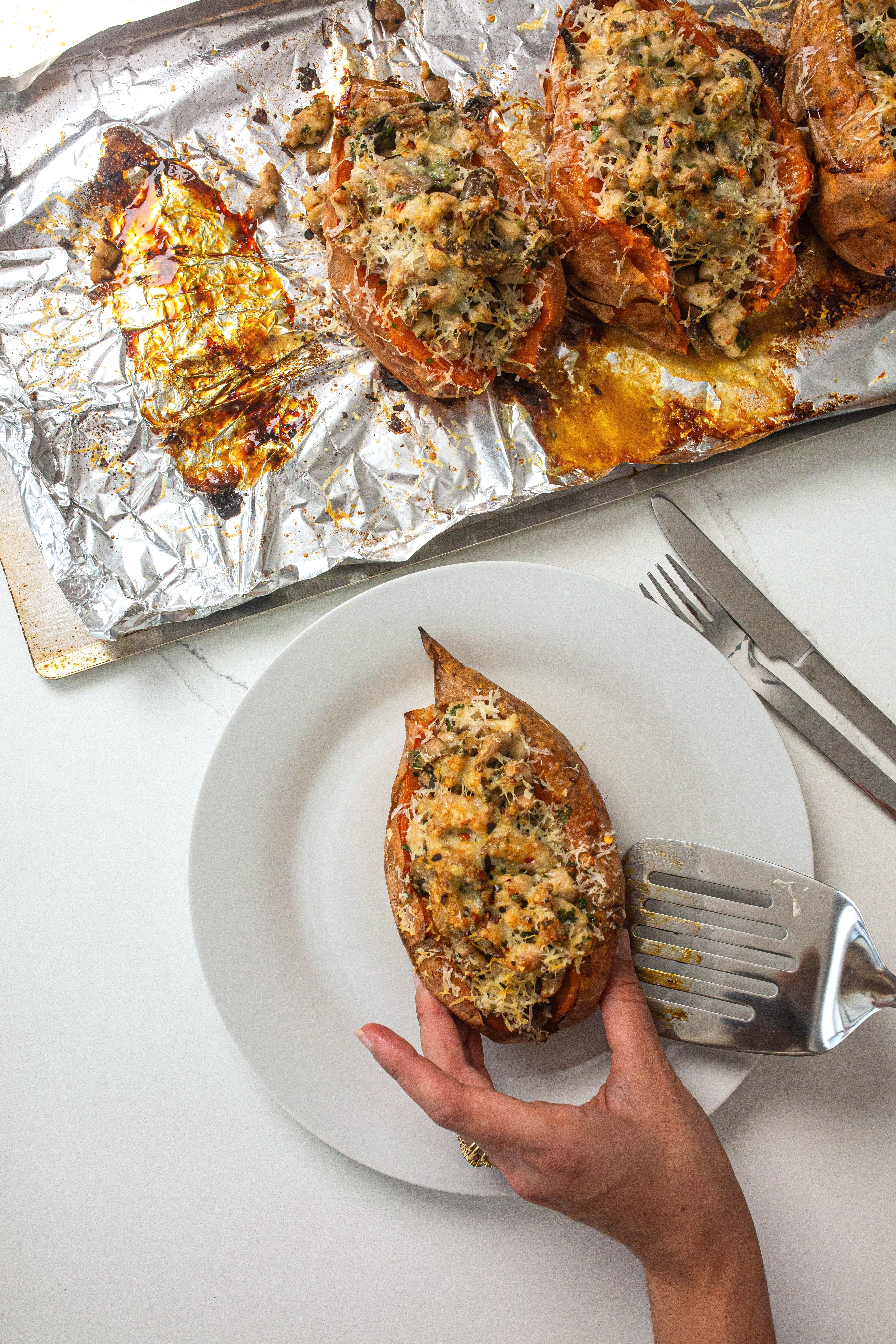 loaded sweet potato is placed on a plate with a spatula from a baking tray with other baked sweet potatoes.