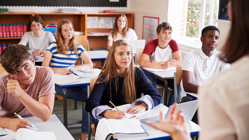 Happy high school students in plain clothes sitting in class and looking at a teacher.