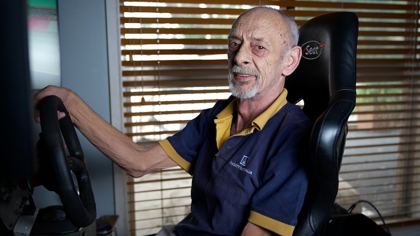 An old man sits in a simulation racing chair.