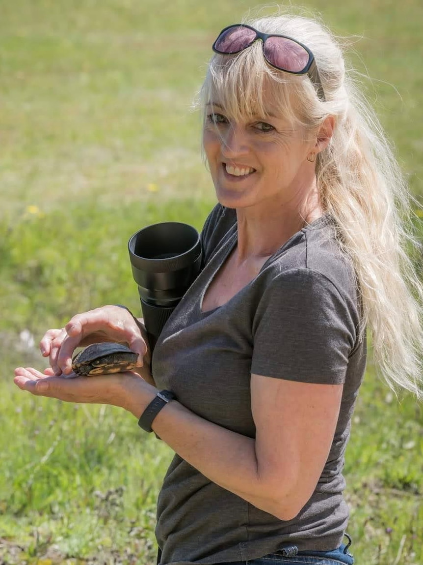 Woman smiles holding a small turtle in one hand. 