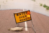 A sign that reads "water on road" in front of flood water
