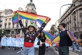Two girls and a boy hold rainbow flags as they march in a pride parade. 