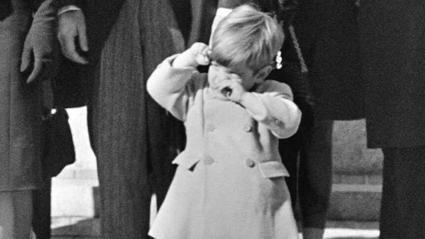 John F Kennedy Jr wipes his eyes at the funeral of JFK.