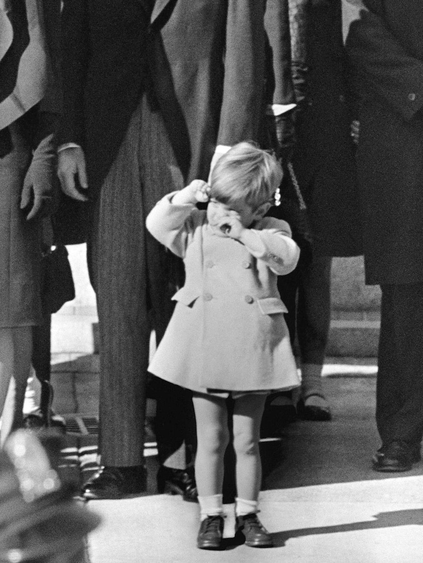 John F Kennedy Jr wipes his eyes at the funeral of JFK.