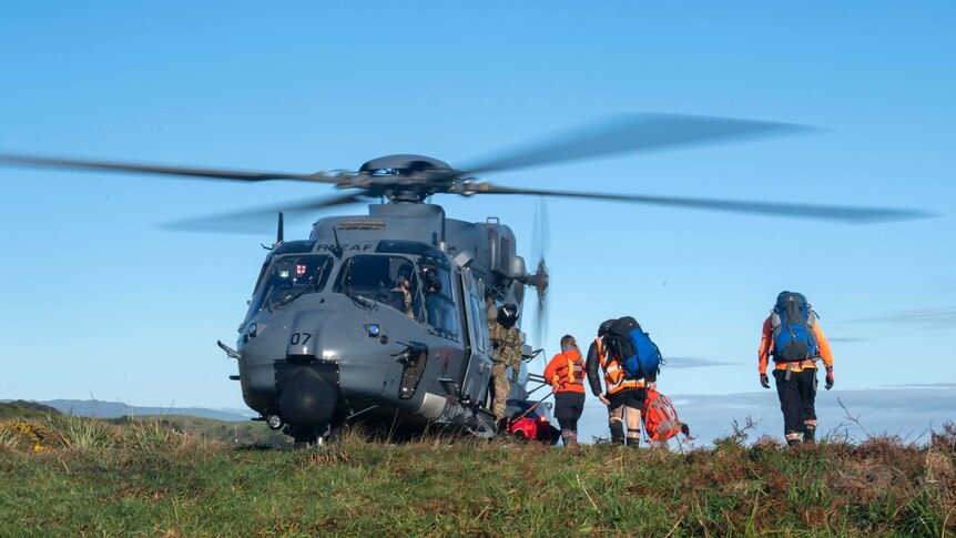 A helicopter waits as search and rescue workers board during a rescue operation.