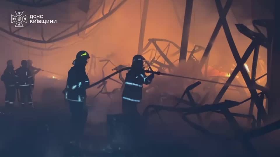 A still-frame image of two firefighters spraying water onto a blaze at night.