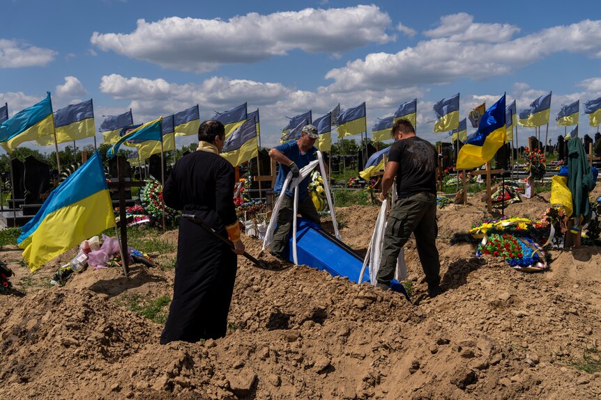 Undertakers lower the coffin of Ukrainian serviceman in dirty patch