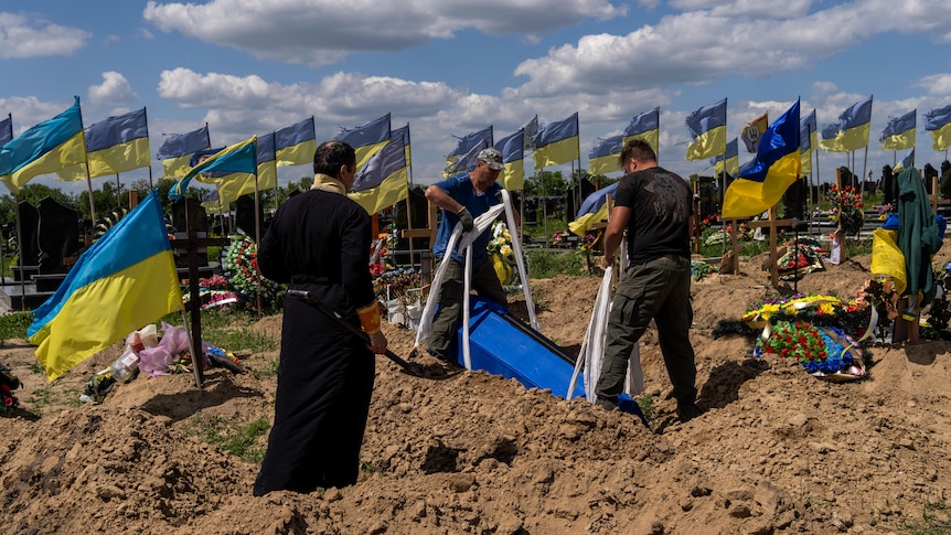 Undertakers lower the coffin of Ukrainian serviceman in dirty patch