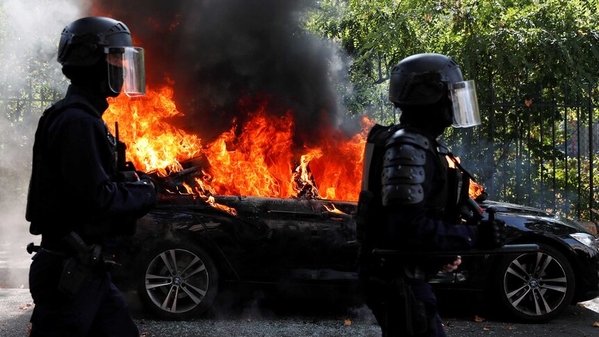 Police in masks walk by burning car