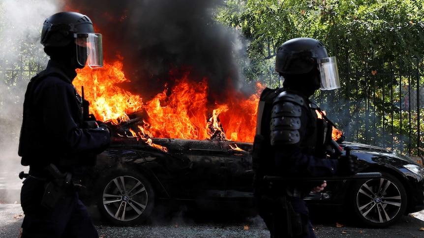 Police in masks walk by burning car