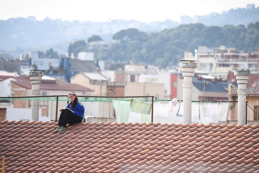 A woman sits by herself reading a book on a rooftop in Barcelona, Spain.