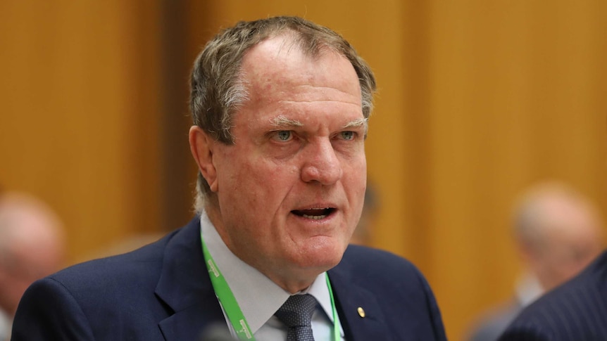 Chris Jordan stares intently while answering a question at Senate Estimates. His brow is furrowed.