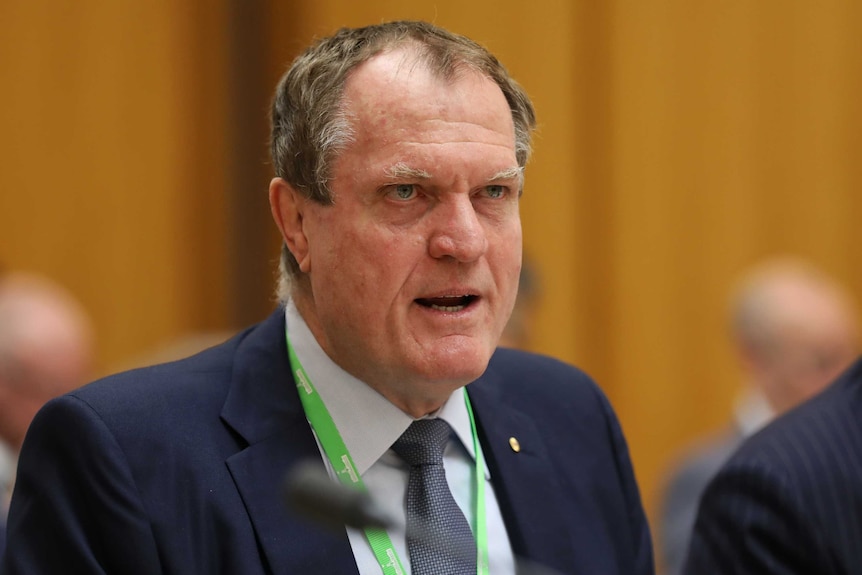 Chris Jordan stares intently while answering a question at Senate Estimates. His brow is furrowed.