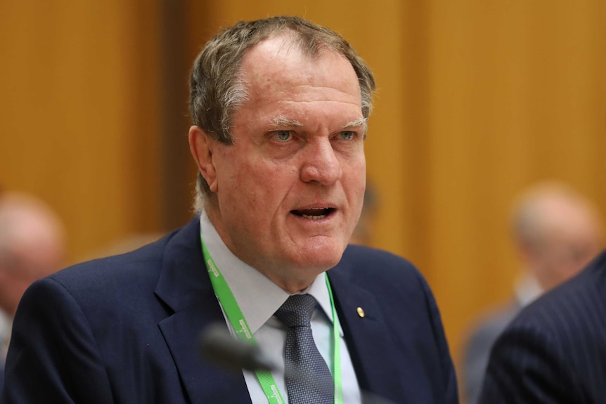 Chris Jordan stares intently while answering a question at Senate Estimates. His brow is furrowed.