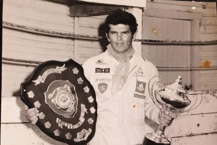 A man stands holding a shield and a trophy