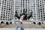 A boy skates in front of a residential complex, with a statue of a woman and horses out the front.