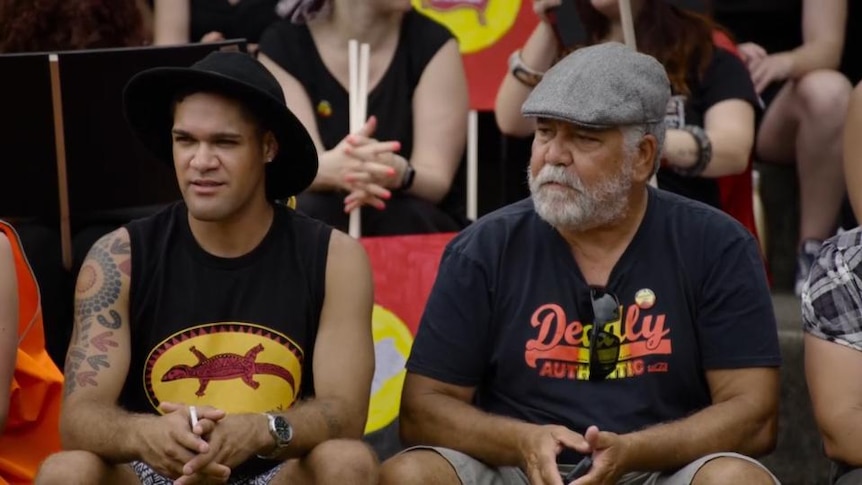 Two indigenous men sit in crowd