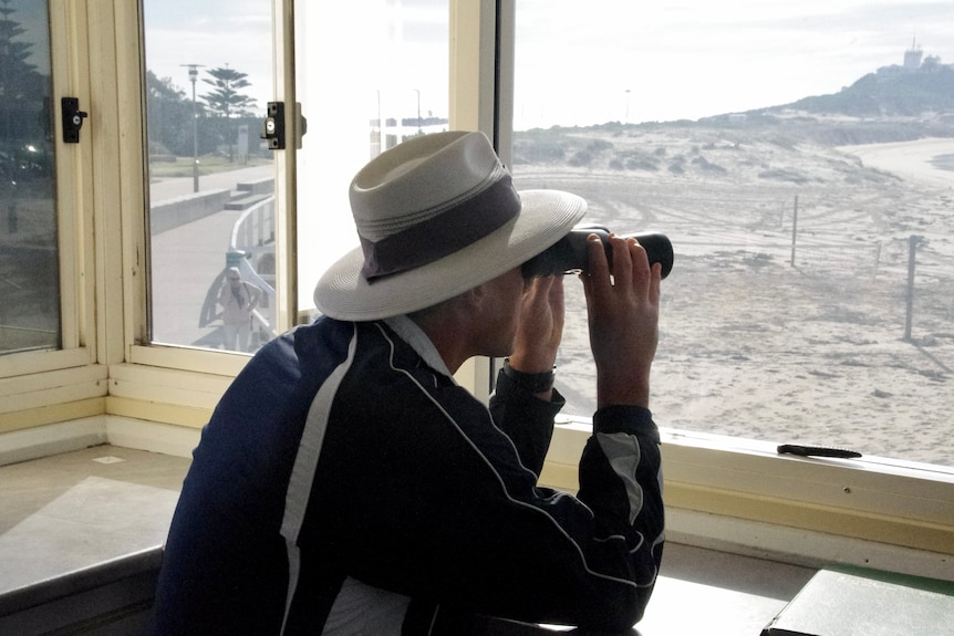 A lifeguard watches the surf with a pair of binoculars.