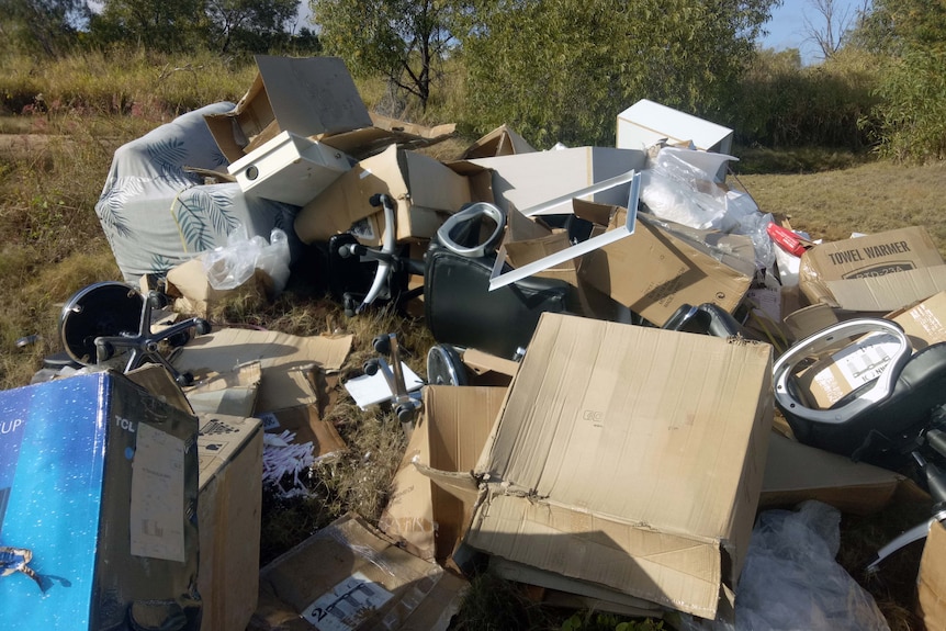 A pile of discarded boxes and furniture in a grassy clearing