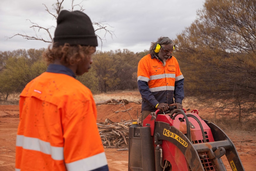 Two men, wearing high-viz shirts, working with mechanical equipment