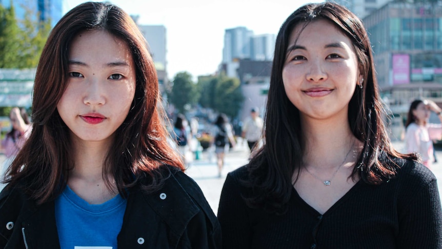 Midshot of two young South Korean women standing in the middle of a university campus.
