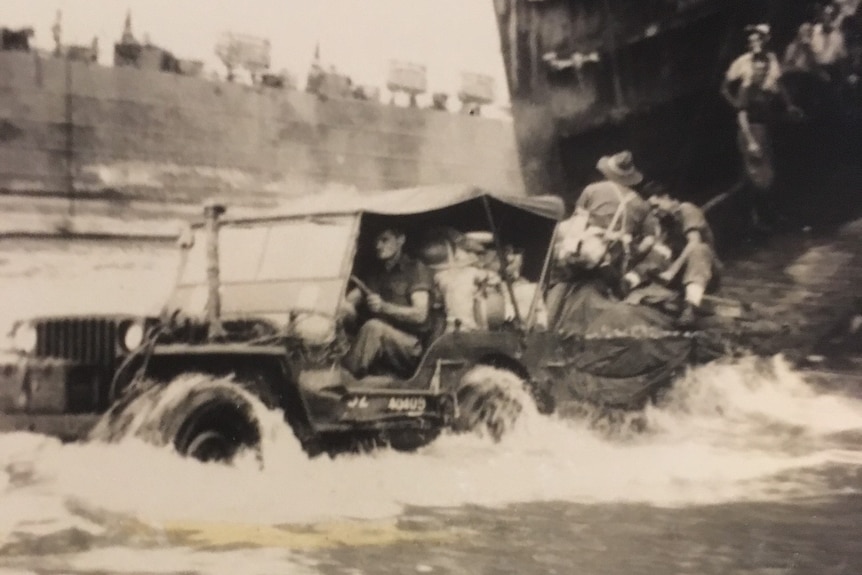 A 1945 black and white image of an open top vehicle moving through the water with soldiers sitting on the back
