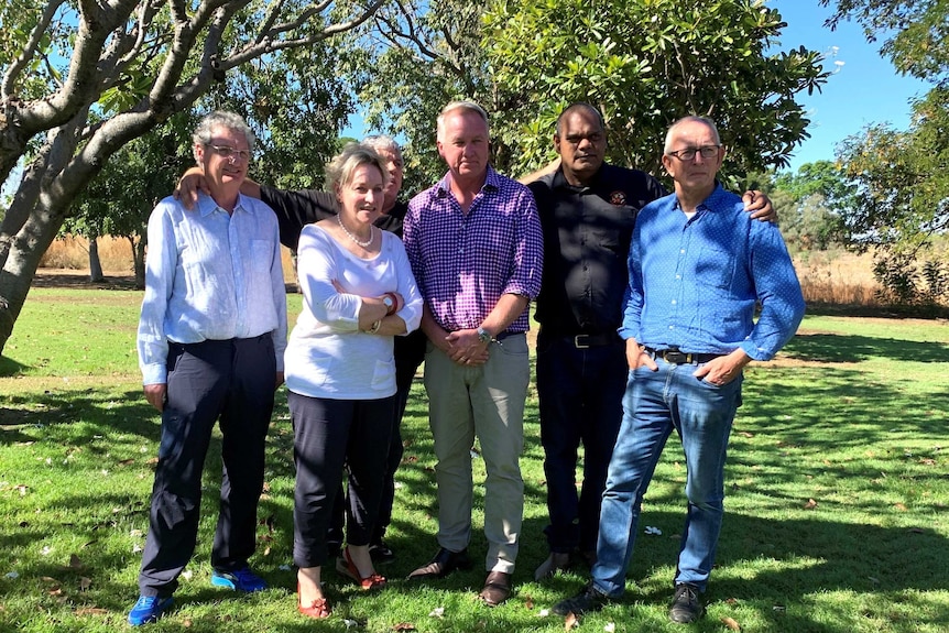 Four men and a woman standing in front of trees.