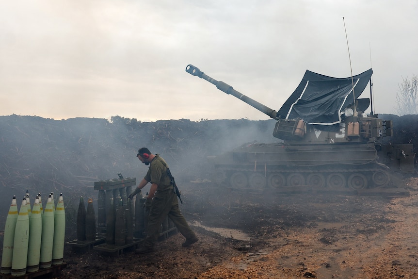 A man inspects artillery shells. He is standing in front of an army tank with its cannon raised