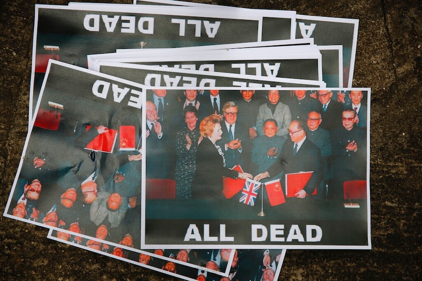 You view a cluster of A4 posters showing a photo of Margaret Thatcher and Deng Xiaoping with the phrase 'all dead' underneath.