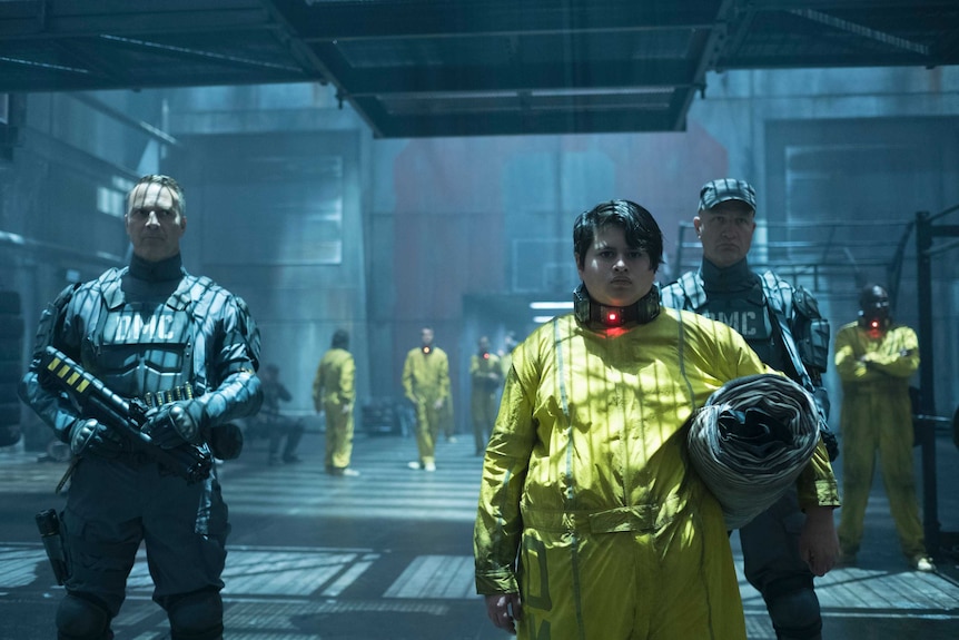 Colour photograph from 2018 film Deadpool 2 of Julian Dennison standing in front of two guards at an industrial prison facility