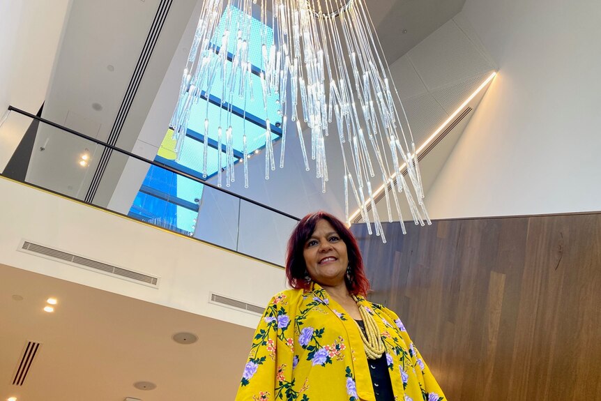 Women in a bright yellow floral jacket smiling underneath a dangling fibre-optic artwork 