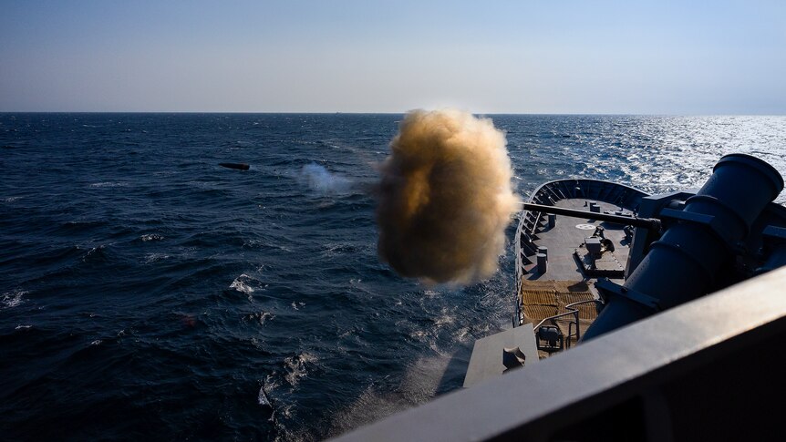 A gun being fired off a boat on the ocean with blue sky above