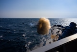A gun being fired off a boat on the ocean with blue sky above